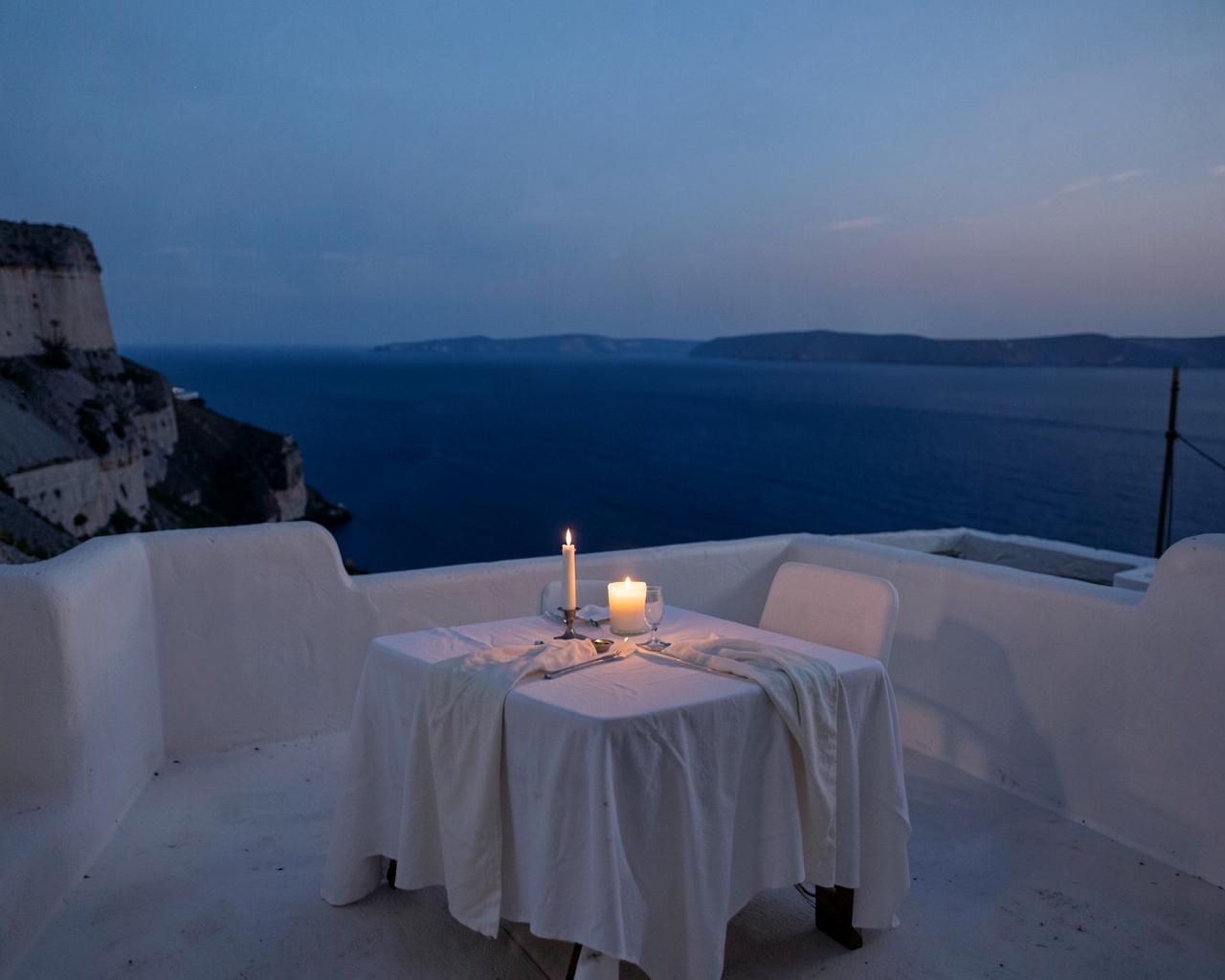 A candlelit table for two on a whitewashed Aegean terrace at dusk